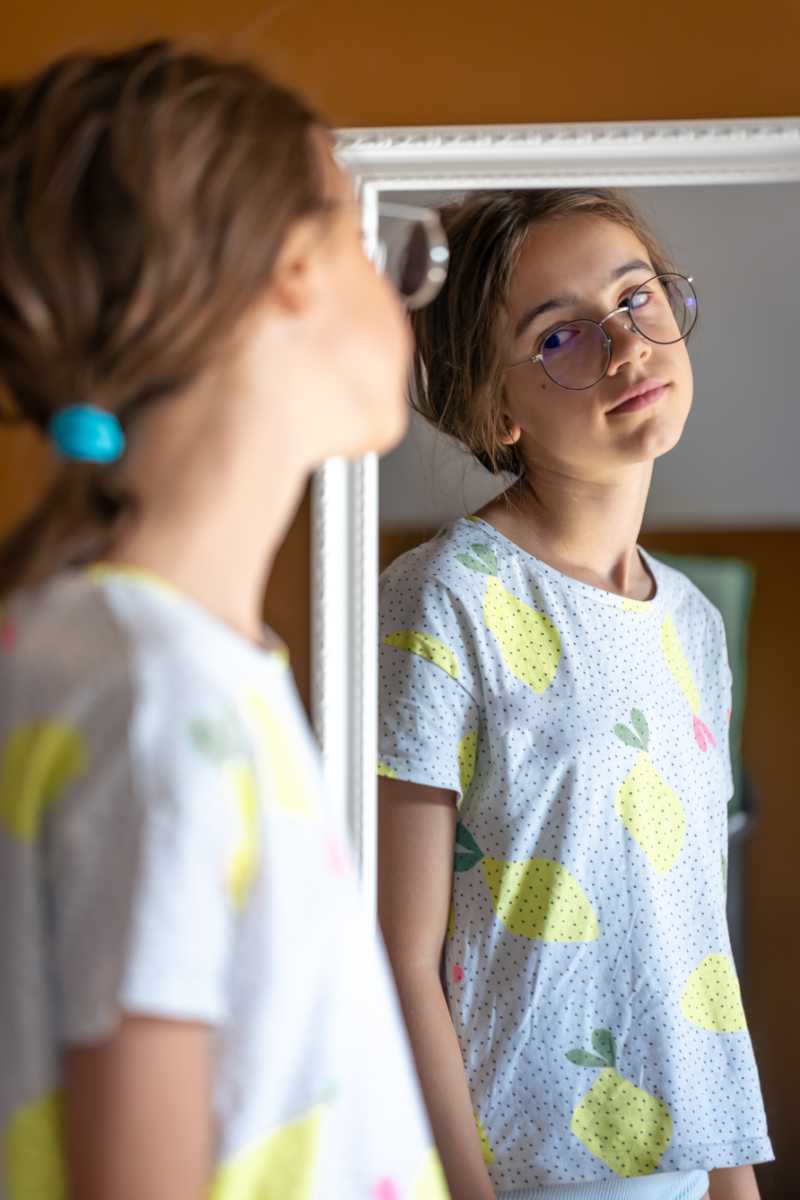 A teenage girl looks at herself in the mirror in the morning.